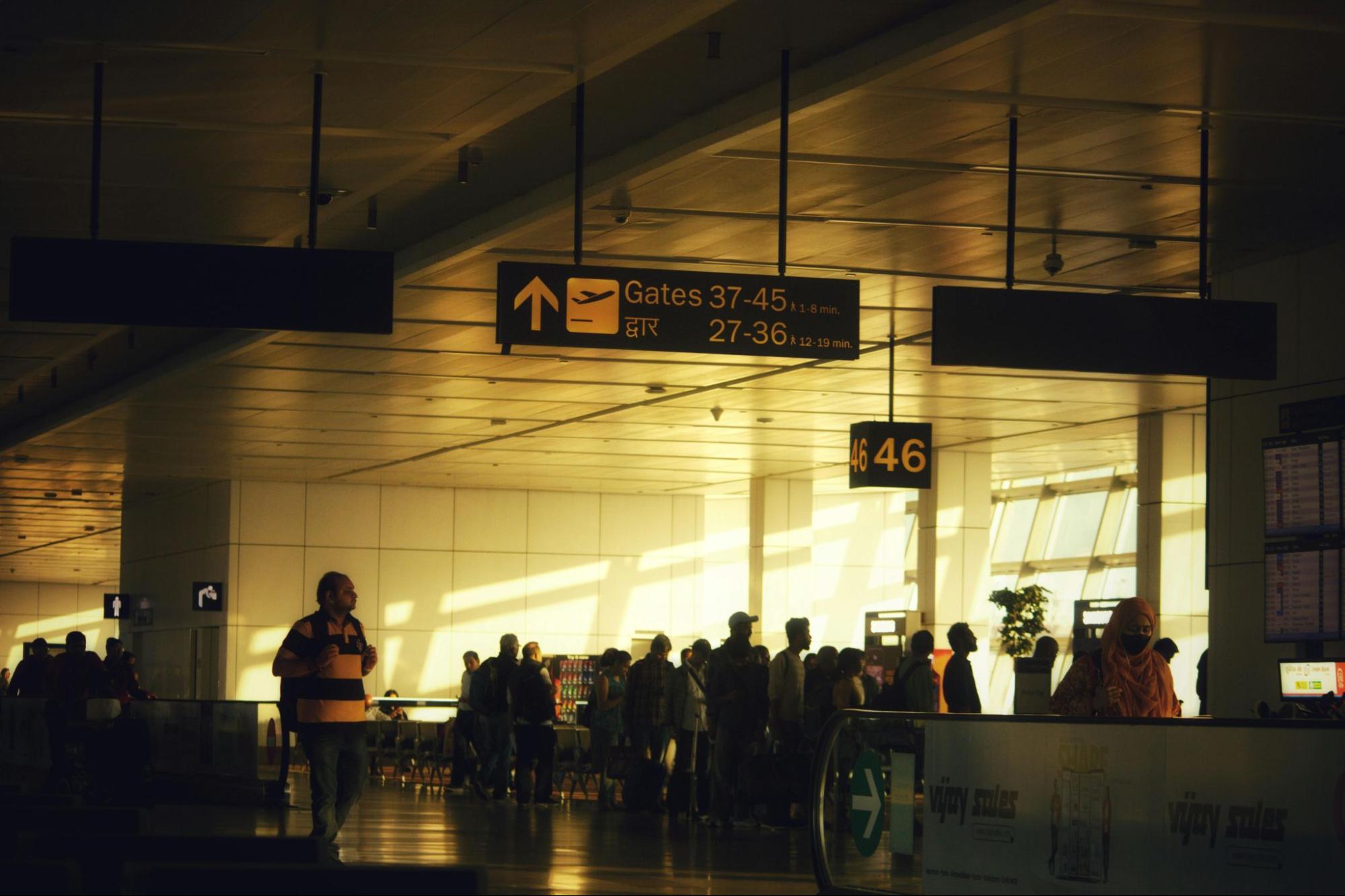 Airport wayfinding signage system displaying directional information for terminal gates 37 to 45 and 27 to 36 with arrow indicators, installed overhead in a modern airport interior under warm ambient lighting, showing clear architectural signage designed for passenger navigation.